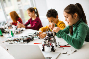 Group of happy kids programming electric toys and robots at robotics classroom